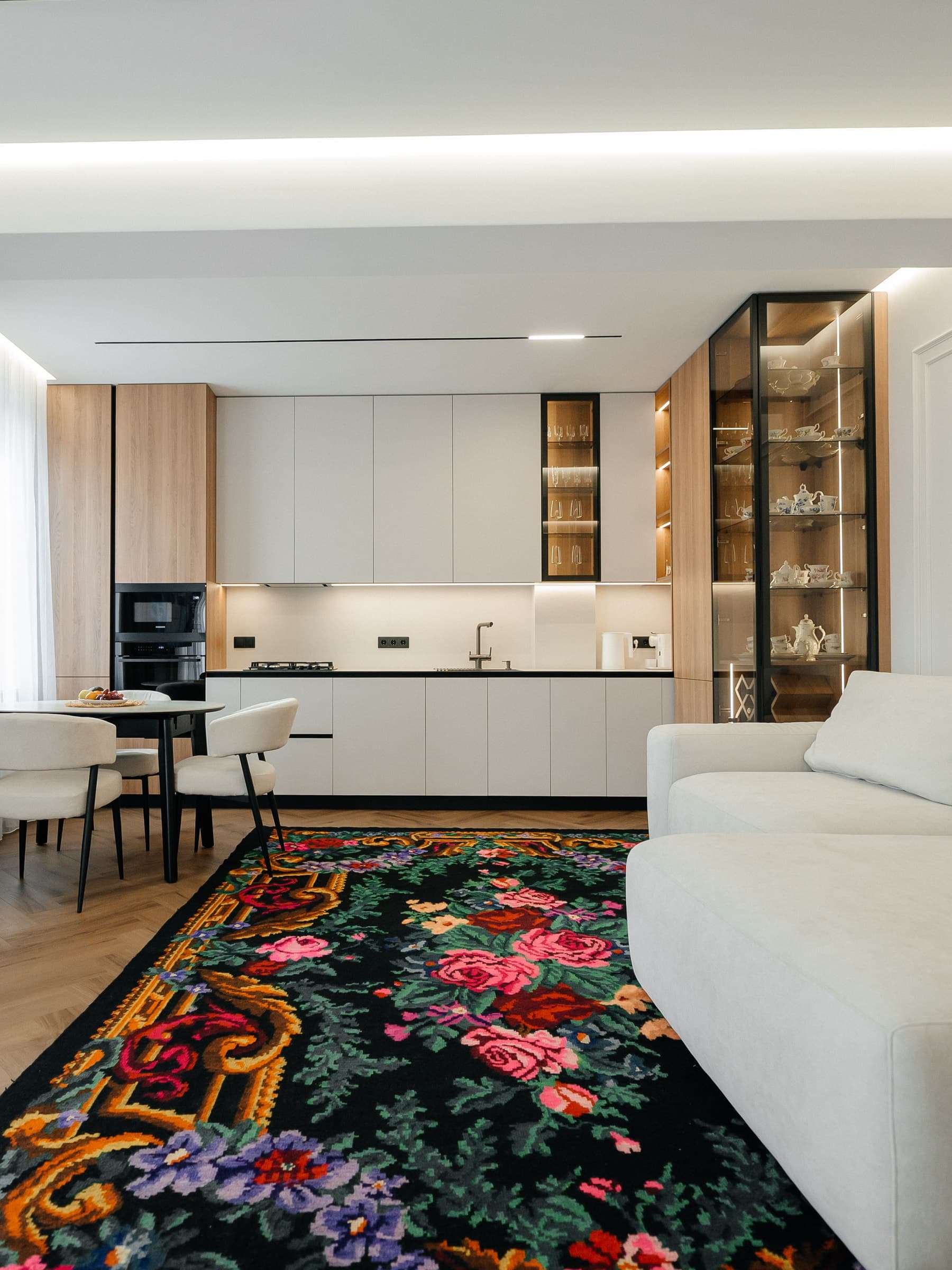 Bulevardul Ștefan cel Mare — Bucătărie albă cu electrocasnice negre și vitrină din stejar cu lumină integrată, deschisă spre living.